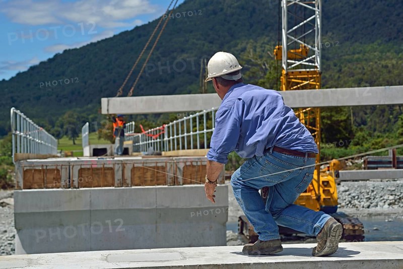 Builders construct a concrete bridge over a small river in Westland, New Zealand