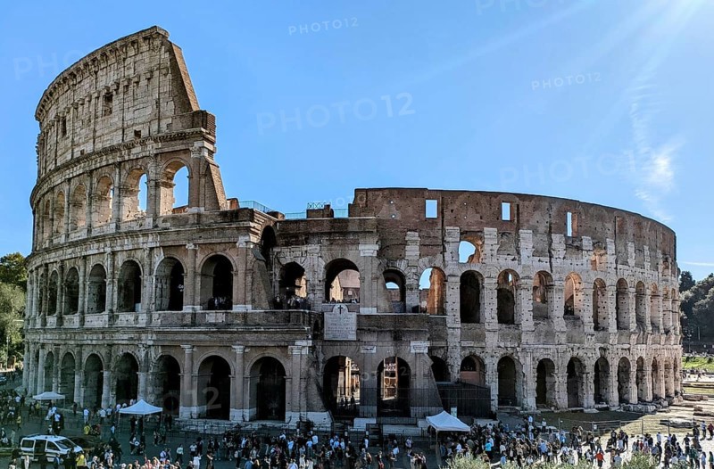 Side view of the Colosseum with tourists visible and sunlight illuminating its arches. Rome, Italy