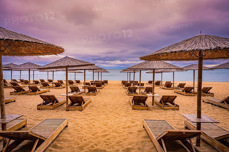 Deserted beach with bamboo umbrellas and sunbeds under a cloudy sky and calm sea, Golden Sands, Varna, Bulgaria