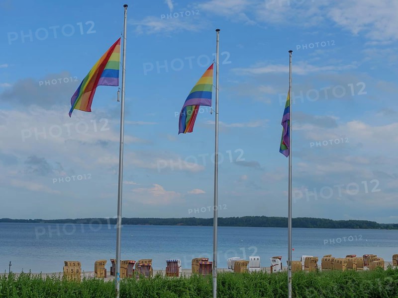 Three rainbow flags waving on the beach above a row of beach chairs, calm water in the background, Eckernförde, schlewsiwg-holstein, germany