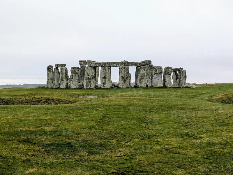 Distant view of Stonehenge surrounded by green grass under an overcast sky. Salisbury, England, United Kingdom