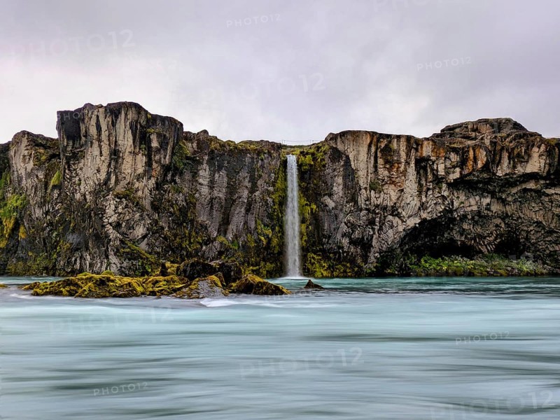 Vibrant waterfall cascading down moss-covered cliffs under a cloudy sky, Icelandic scenery. Iceland