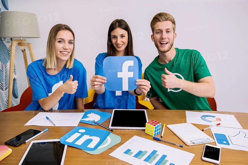 Smiling woman holding facebook logo with his friends showing thumbup sign