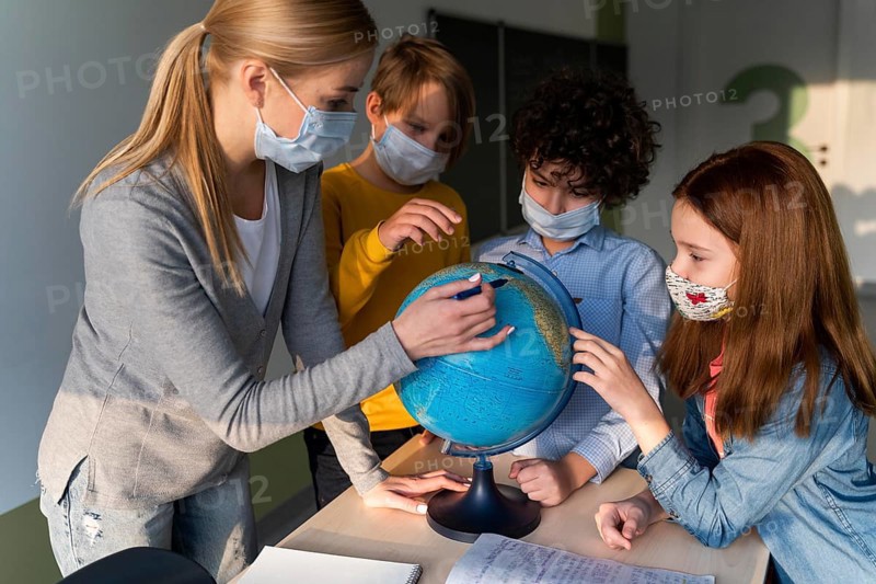 Female teacher with medical mask teaching geography with earth globe class