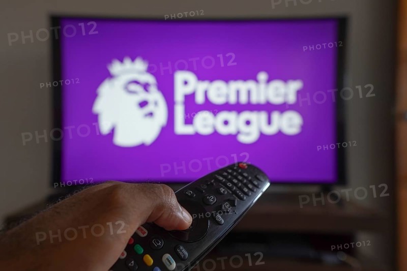 May 14, 2024, Brazil. In this photo illustration, a hand holding a TV remote control in front of the Premier League logo on a TV screen