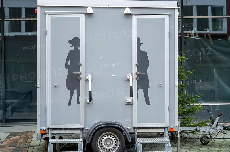 Modern portable toilet trailer with separate entrances for men and women, featuring elegant victorian silhouettes