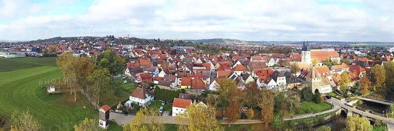 This aerial photo shows the picturesque town of Herrieden. At the centre are the red roofs of the closely spaced buildings, which represent the typical townscape of a small Bavarian town. The autumn colours of nature lend the image a warm and inviting atmosphere, while the view beyond the town reveals a beautiful landscape. Herrieden, Middle Franconia, Bavaria, Germany