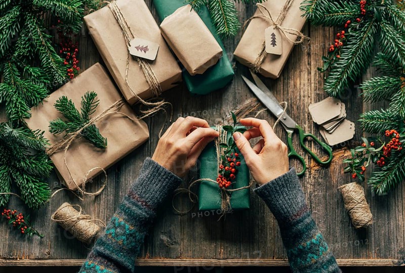 Die Hände einer nicht erkennbaren Frau verpacken Weihnachtsgeschenke auf dem Tisch in einer Kreativwerkstatt