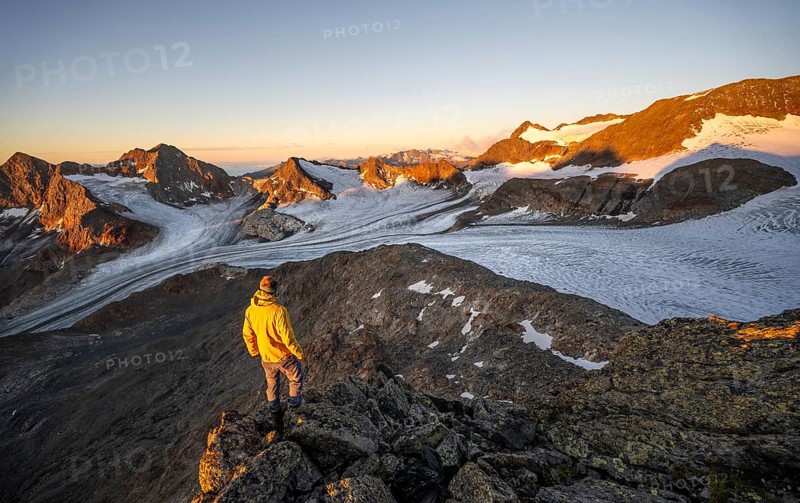 Mountaineers in front of a picturesque high mountain landscape at sunrise with alpenglow, glacier and rocky mountain peaks in the morning light, view at the Becher on mountain peaks Königshofspitz and Sonklarspitze and Schwarzwandspitz with glacier Übeltalferner, Stubai Alps, South Tyrol, Italy