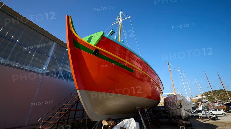 Side view of an orange-coloured boat in a shipyard under a blue sky, Diakofti boatyard, new construction of a coloured wooden boat, Diakofti, Patmos, Dodecanese, Greek Islands, Greece