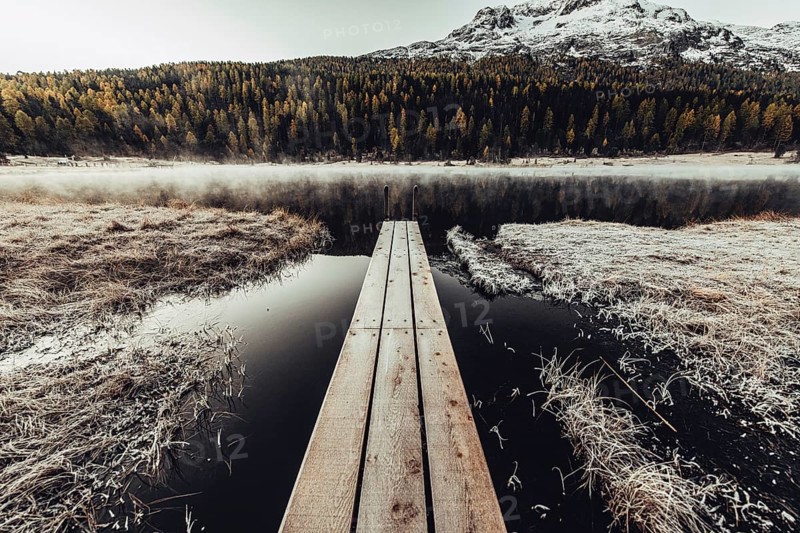 Lake Staz near Sankt Moritz in the Engadin in Switzerland. Morning atmosphere with fog in autumn. Water reflection and snow-covered mountains in the background