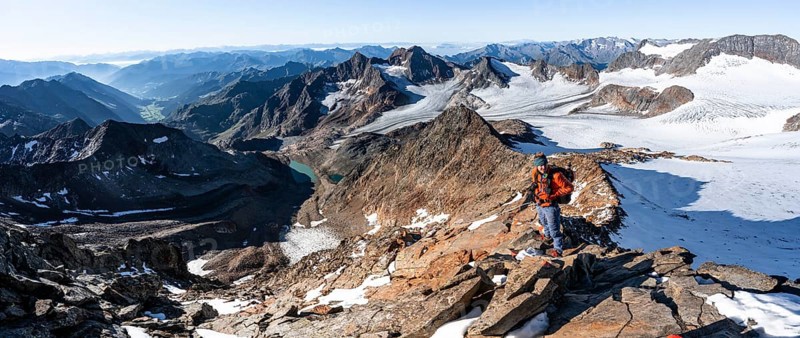 Mountaineer on a rocky ridge on the Wilder Freiger summit, behind him Signal summit and Becher summit with Becherhaus, picturesque high mountain landscape, view of Übeltalferner glacier and rocky mountain peaks Königshofspitz and Sonklarspitze, Stubai Alps, South Tyrol, Italy