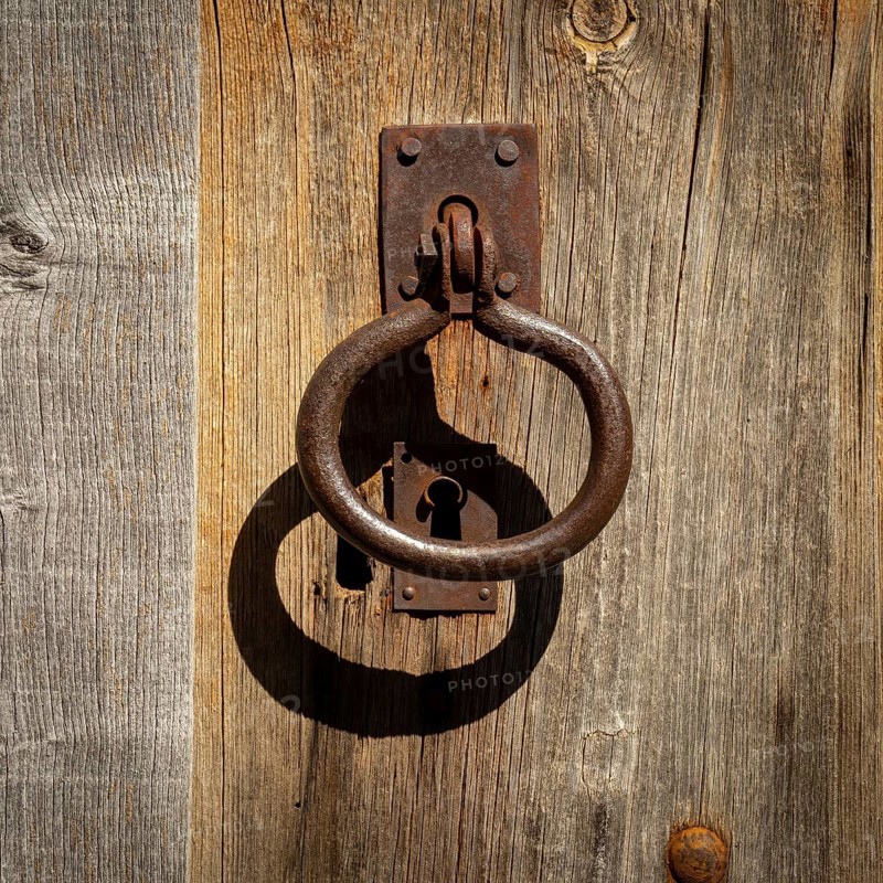 A weathered wooden door showcases an ornate metal knocker and an antique keyhole, reflecting the charm of traditional craftsmanship. The rustic textures add character and history