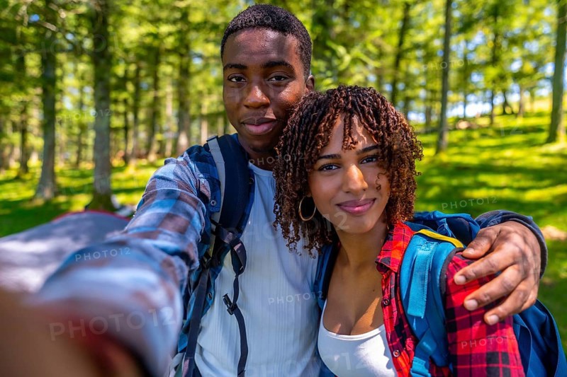 Young hikers with backpacks enjoying a sunny summer day, capturing a joyful selfie portrait amidst the vibrant green forest