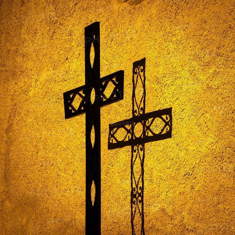 Shadow cast by one ornate cross on a textured wall at sunset illuminates the religious significance and artistry of faith. Auvergne. France