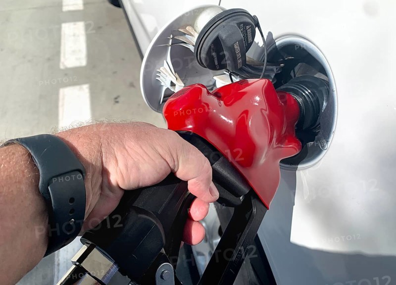 Male hand holding gas pump nozzle pumping gas into vehicle