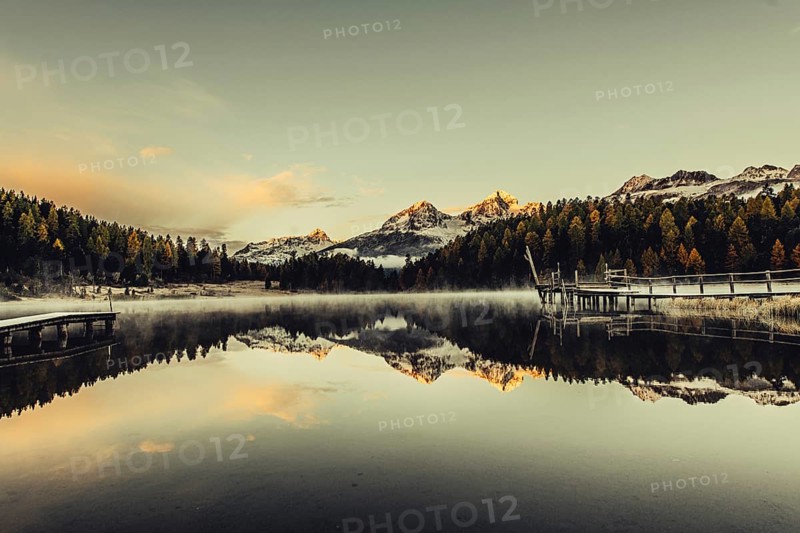 Lake Staz near Sankt Moritz in the Engadin in Switzerland. Morning atmosphere with fog in autumn. Water reflection and snow-covered mountains in the background