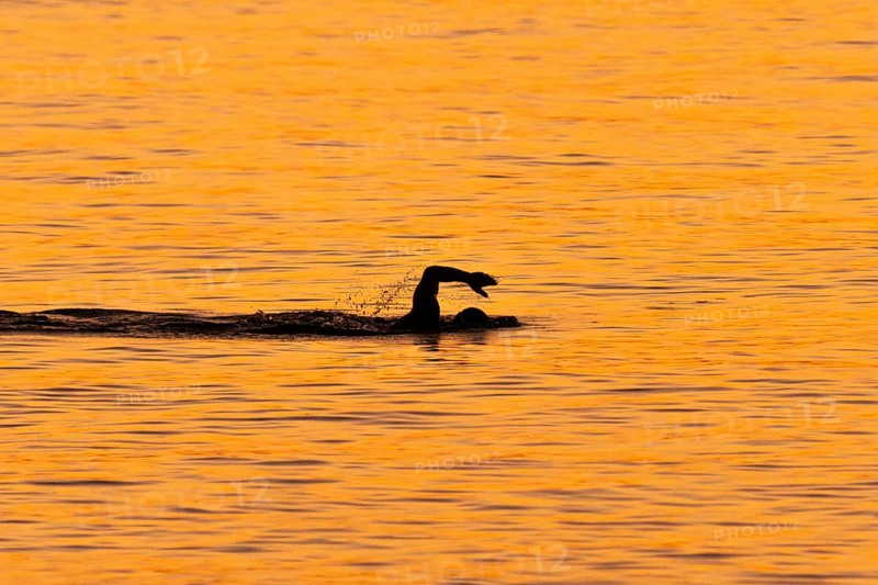 A man swims at sunrise on the Costa Rei, a coastline of the Italian island of Sardinia, in the Mediterranean Sea, Monte Nai, Costa Rei, Sardinia, Italy