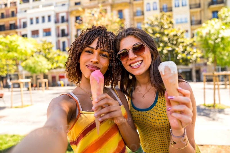 Two happy female friends enjoying ice cream cones on a sunny day in the city, taking a selfie to capture the moment