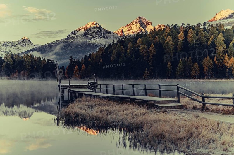 Lake Staz near Sankt Moritz in the Engadin in Switzerland. Morning atmosphere with fog in autumn. Water reflection and snow-covered mountains in the background