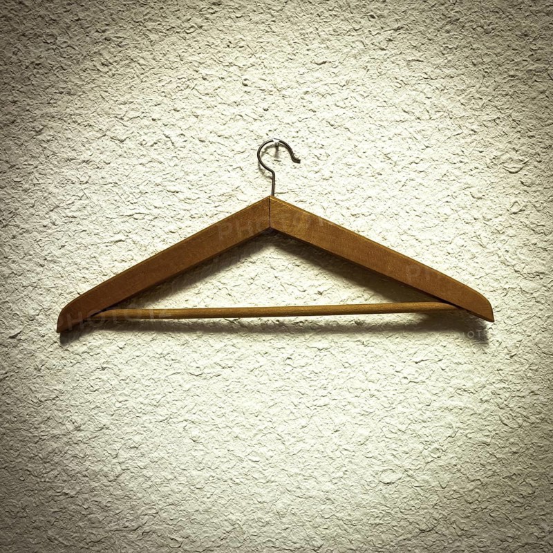 A wooden clothes hanger is resting on a textured wall, showcasing its natural finish and design. The scene emphasizes minimalism, highlighting practicality in home organization