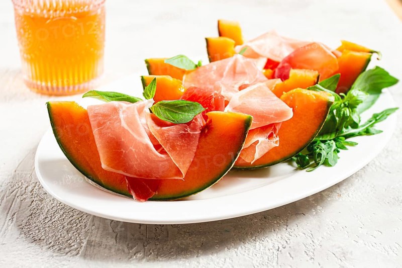 Cantaloupe melon with prosciutto and fresh basil, on a white plate, natural light