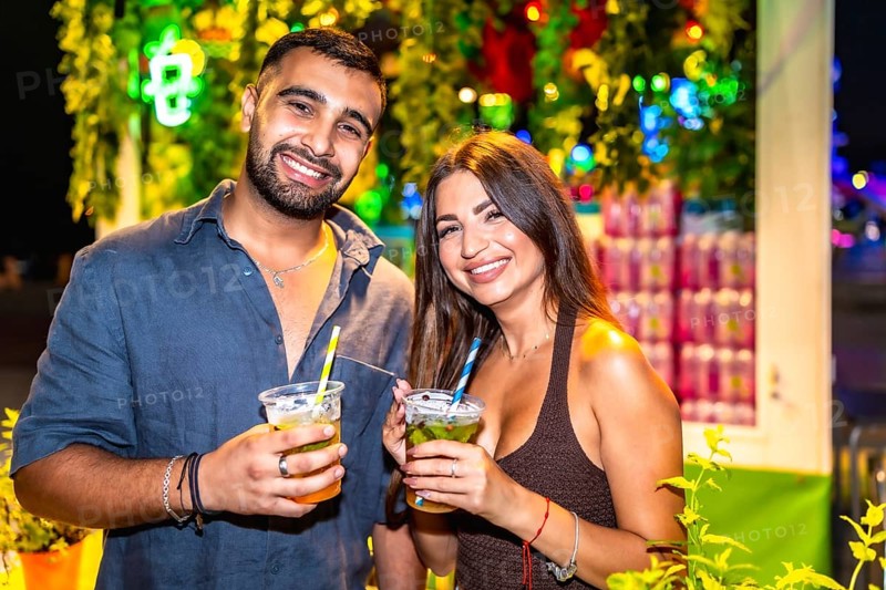 Young couple smiling and holding cocktails at a night market, enjoying the vibrant atmosphere and refreshing drinks