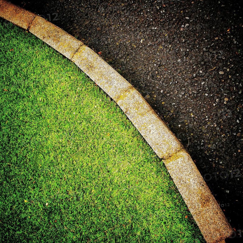 The vibrant green grass curves smoothly alongside a dark asphalt pathway, creating a pleasing contrast in an urban environmental setting during the daytime