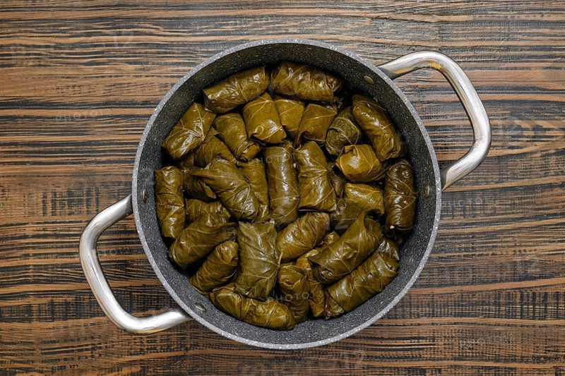 Each dolma is carefully rolled with seasoned rice and spices wrapped in grape leaves. The pot is filled with these savory bites, ready to be cooked to perfection in the cozy kitchen