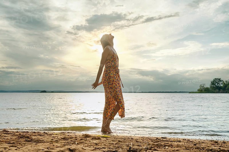 Woman enjoying serenity by the lakeside at sunset with vibrant dress flowing in the breeze