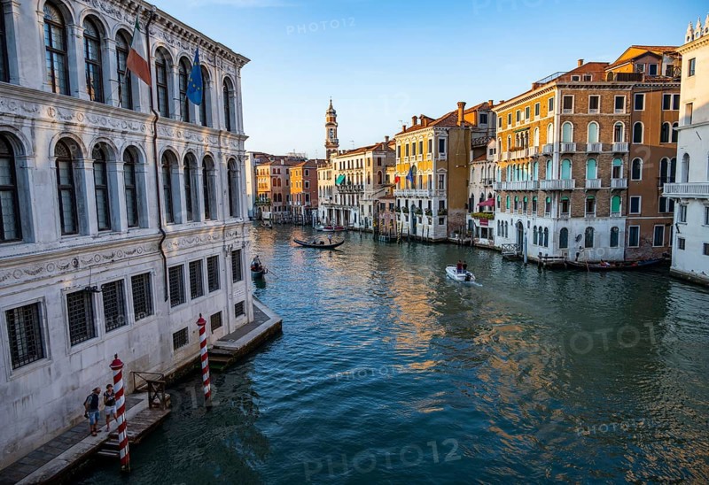 View of the Grand Canal with gondoliers at sunset, picturesque evening mood with palazzos on the canal and church tower of the Chiesa Parrocchiale dei Santi Apostoli, view from the Rialto Bridge, Venice, Veneto, Italy