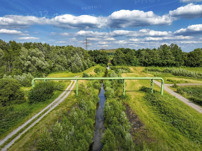 Bottrop, North Rhine-Westphalia, Germany - Renaturalised Boye, the tributary of the Emscher, has been transformed into a near-natural watercourse, flood protection through newly designed flooding areas, the Boye is now free of wastewater following the construction of a parallel sewer, is part of the Emscher river system and thus part of the Emscher conversion, was previously an open, above-ground wastewater channel, mixed water channel with surface water and wastewater. Wind turbine on the Mottbruch spoil tip at the back