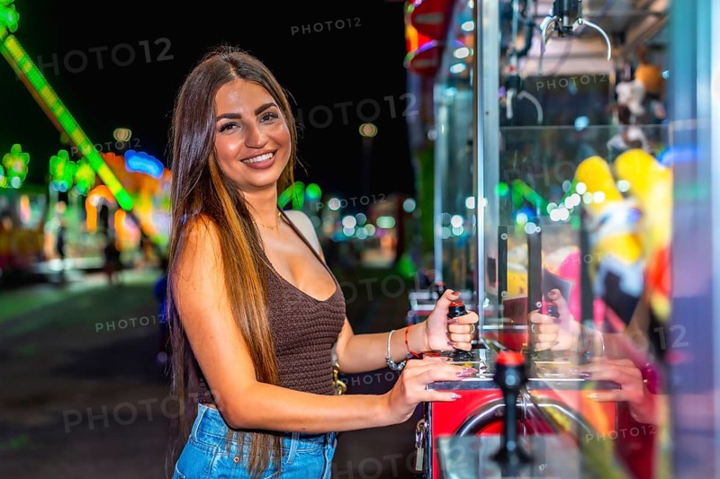 Happy young woman enjoying playing a claw crane game at an amusement park, trying to grab a prize with the mechanical claw