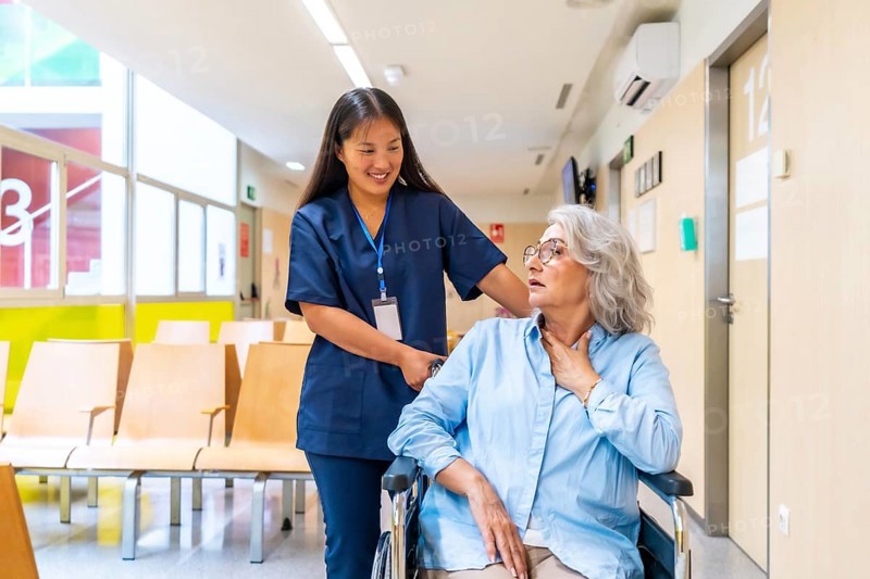 Young nurse supporting elderly woman experiencing respiratory problems in wheelchair, providing care and navigating hospital hallway
