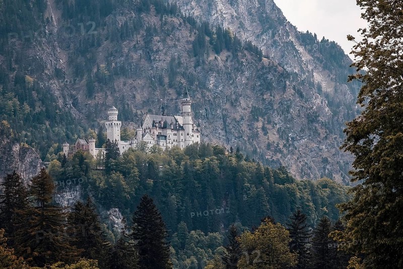 The awe-inspiring Neuschwanstein Castle is situated on rocky, wooded terrain against a dramatic mountain backdrop, Schwangau, Bavaria