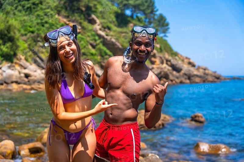 Interracial couple wearing snorkeling gear pointing at crystal clear tropical sea, ready for summer adventure