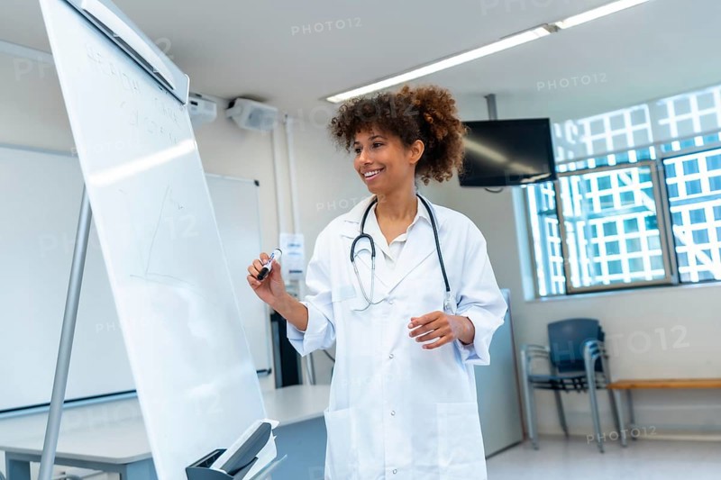 Female medical professional explaining a concept drawing on a whiteboard during a medical lecture in a hospital conference room