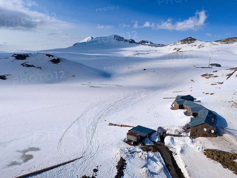 Snow-covered huts lie in a peaceful mountain landscape under a blue sky, aerial view, Aragaz, Aragac, Alagyaz, extinct stratovolcano, 4090 m, Aragazotn, Shirak, Armenia