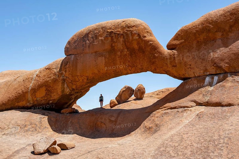 Tourist in a rock arch, round rock formations with stone arch, Pontok Mountains, Great Spitzkoppe, Spitzkoppe, Great Spitzkoppe Nature Reserve, Namibia