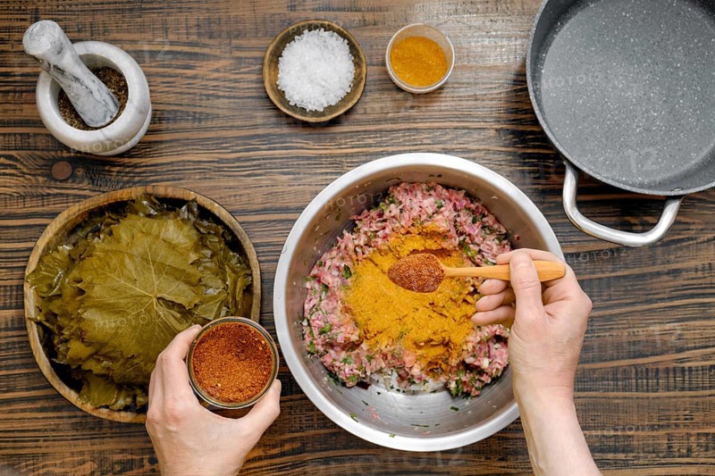 Home cook prepares dolma by adding pepper mix into minced meat. Pickled grape leaves are ready for wrapping, creating a traditional Georgian dish with rich flavors