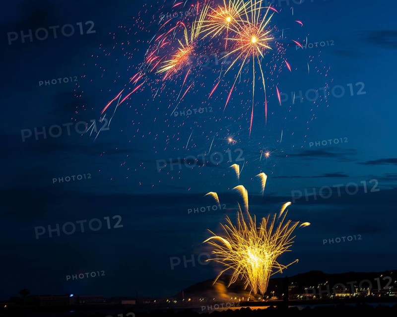 A brilliantly radiant, atmospheric firework display for the Heligoland island festival in red and gold over the night-time lowlands, inland harbour, jetty and lobster shacks, with the reflecting waters of the North Sea in front, golden-coloured fire fountain and three whirling stars, Night sky at the island festival in summer, symbolic image also for New Year's Eve, New Year's Eve fireworks, bright, colourful, many colourful traces of light, sparks, lively glitter, night, Heligoland Island, Schleswig-Holstein, Germany