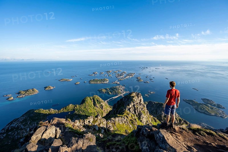 View of numerous small rocky islands with houses, mountaineers on the summit of Festvågtind, view of Henningsvær, Vågan, Lofoten, Nordland, Norway