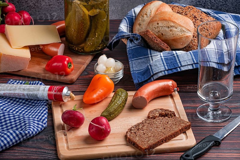Rustic arrangement with sausage, cheese, vegetables, mustard and bread on a laid table