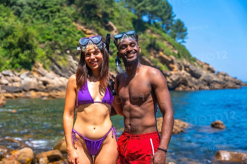 Interracial couple smiling and wearing snorkeling gear at a beautiful beach getting ready to snorkel
