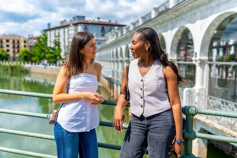 Two female tourists enjoying a summer day in bayonne, france, chatting on a bridge over the nive river