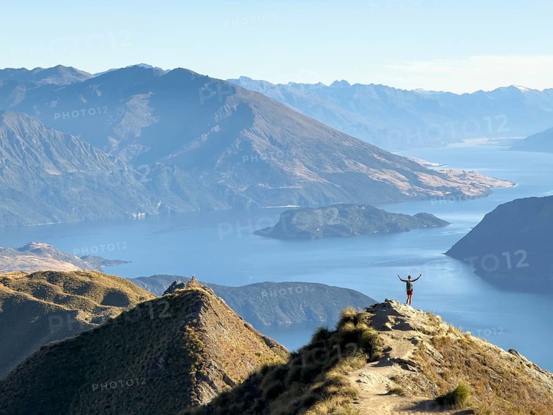 Person with outstretched arms on the hiking trail to Roys Peak Lookout, Lake Wanaka, Wanaka, South Island, New Zealand, Oceania