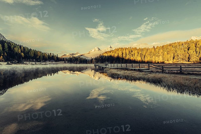 Lake Staz near Sankt Moritz in the Engadin in Switzerland. Morning atmosphere with fog in autumn. Water reflection and snow-covered mountains in the background