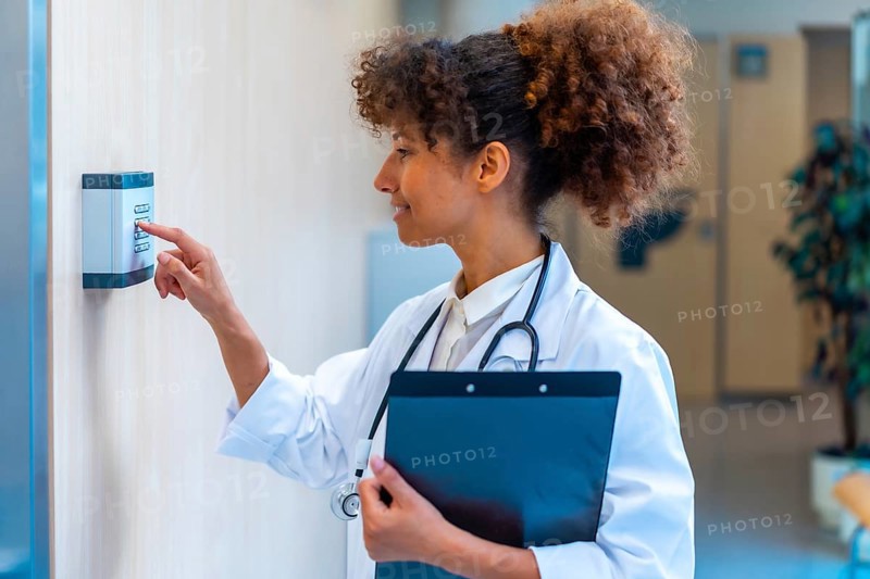 Confident female doctor using a keypad to enter a code, holding a clipboard in a hospital corridor