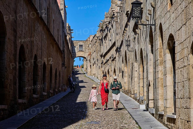Tourists walking through a sunny, stony alley, Knights Street, Rhodes Old Town, Rhodes, Dodecanese, Greek Islands, Greece