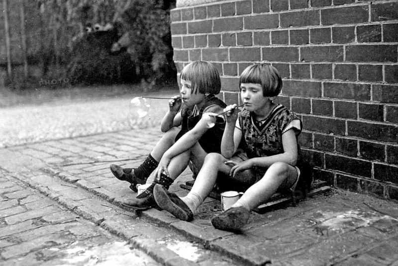 Two girls playing with soap bubbles, 1920s, Two children sitting on a brick wall and blowing soap bubbles. Relaxed atmosphere, historical photo